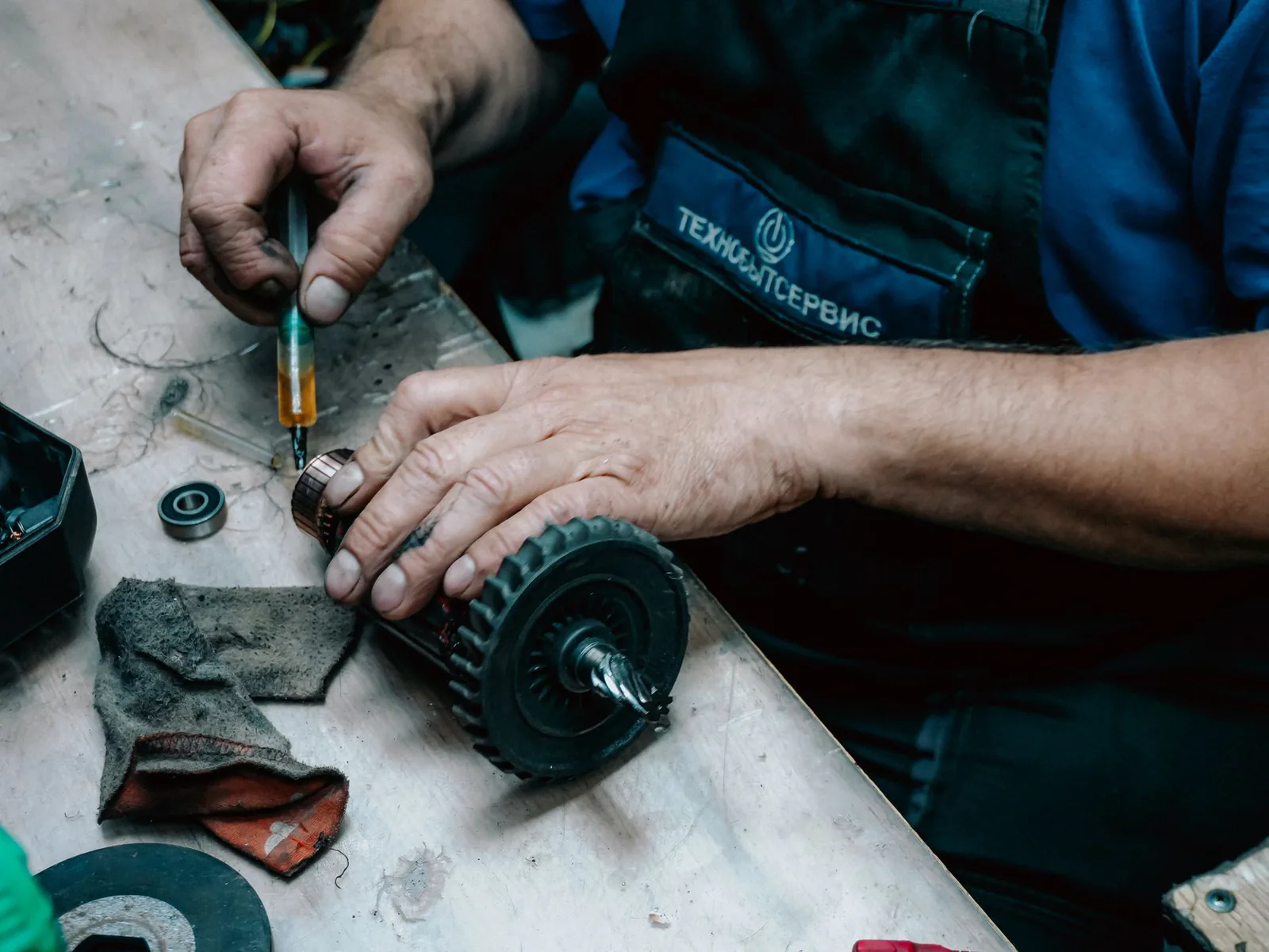 Mains d'un technicien qui graisse l'induit d'un moteur électrique posé sur un établi