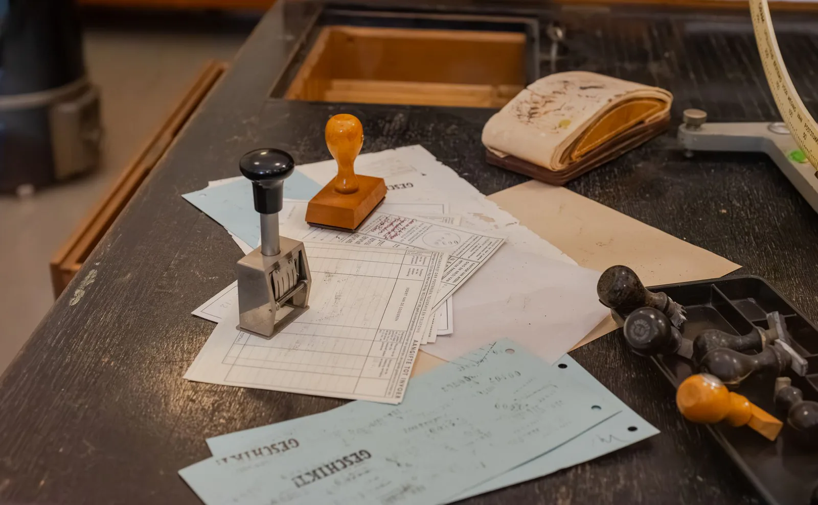 Printed forms and carbon copies spread on a dark desk with two rubber stamps and an ink pad