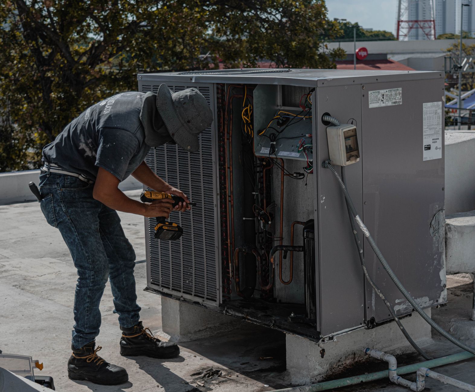 Technicien démontant un groupe de climatisation sur une toiture avec une visseuse