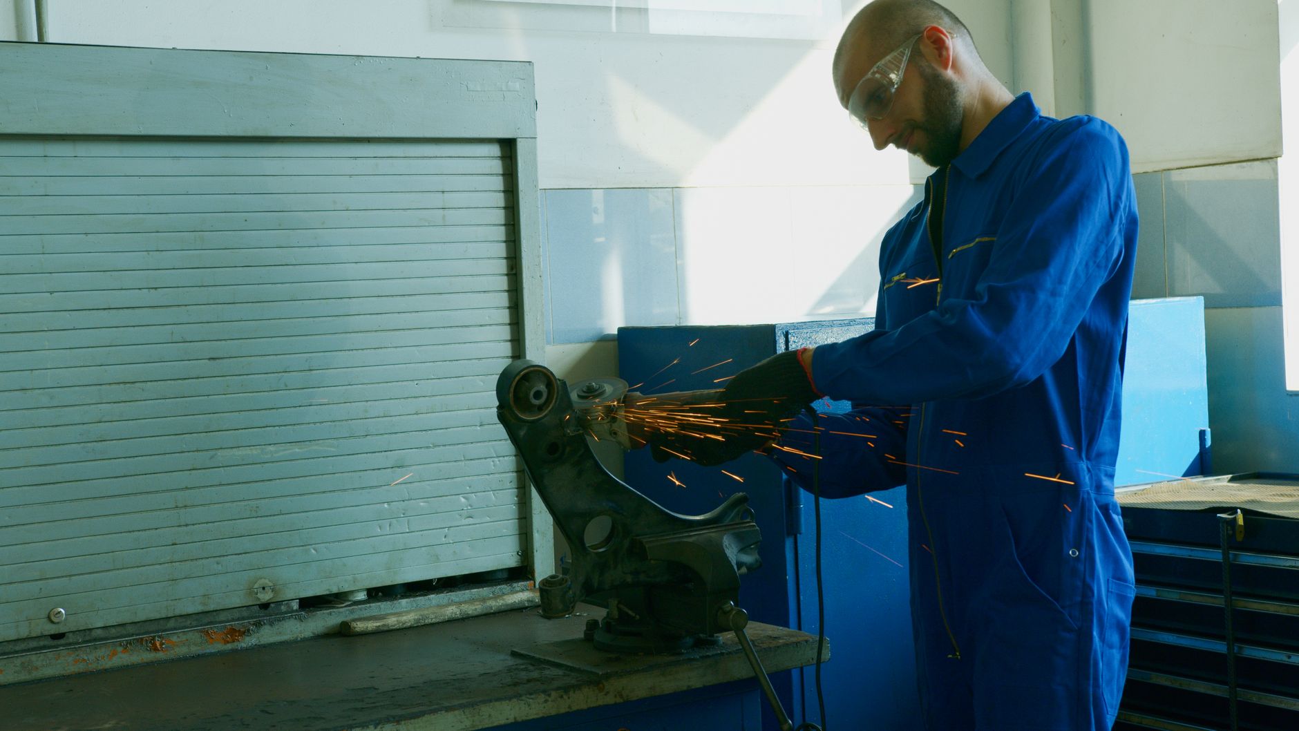 Technicien en combinaison meulant une pièce métallique dans une gerbe d'étincelles