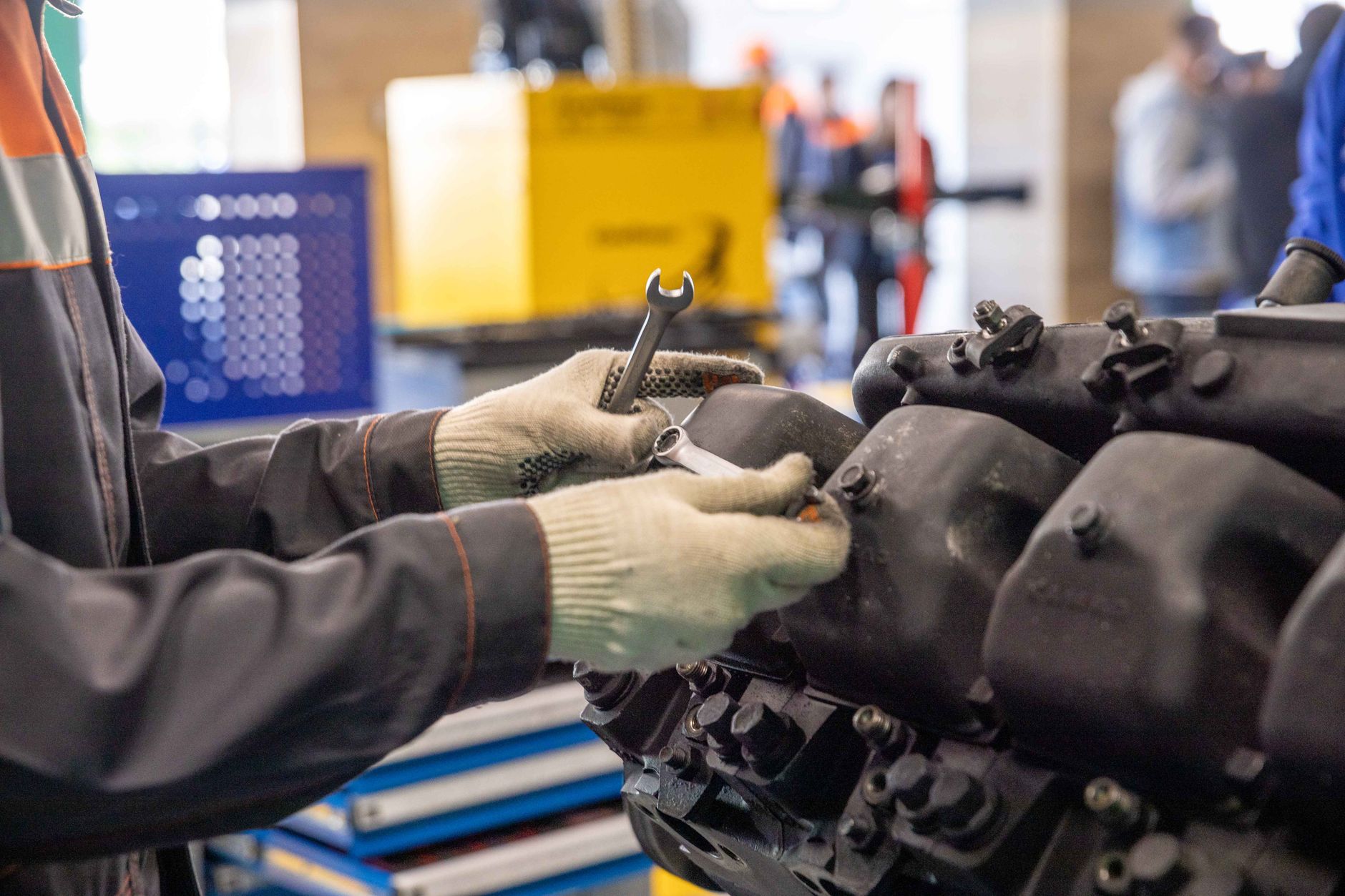 Mains gantées tenant une clé plate sur un moteur démonté dans un atelier